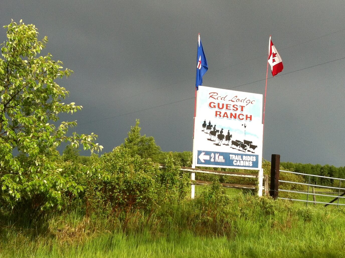 Red Lodge Guest Ranch sign Outdoor sign for Red Lodge Guest Ranch showing horseback riders and cattle under a dark sky.