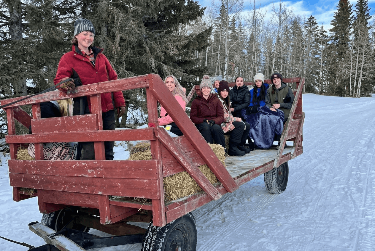 group-sleigh-ride-on-snowy-trail A group of people riding in a wooden wagon on a snowy trail.