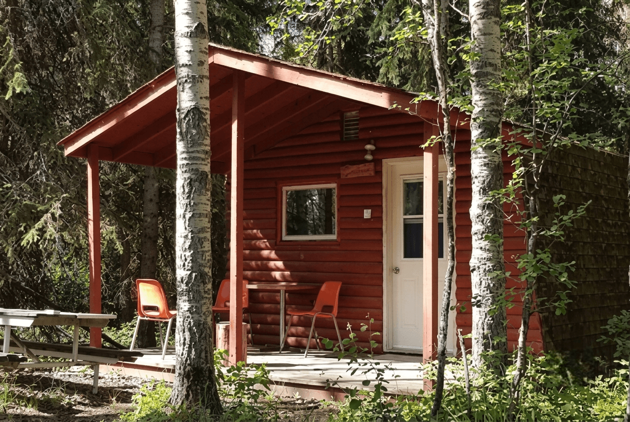 large cabin Red wooden cabin with front porch and chairs nestled among trees.