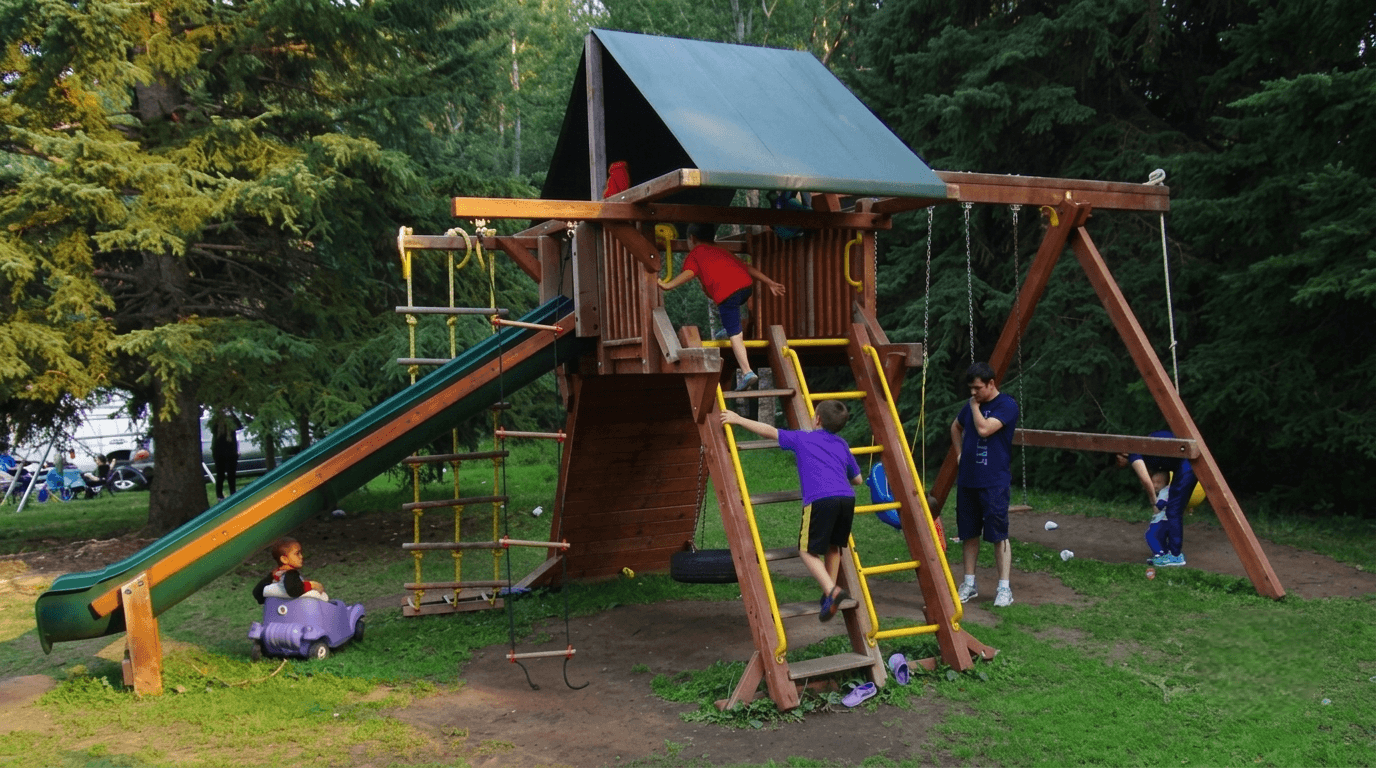 playground Children playing on a wooden playground structure with slide and swings in a park.