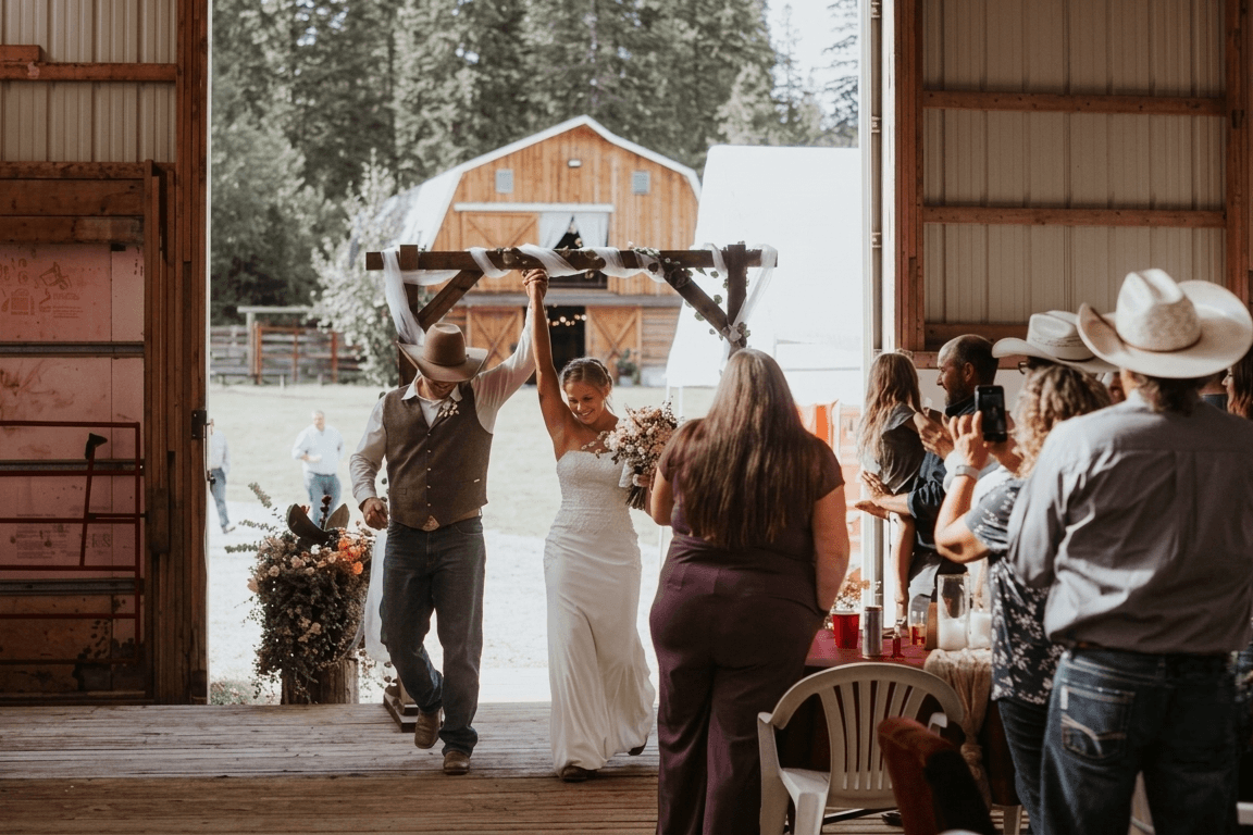 wedding-hall Bride and groom walking hand-in-hand through a barn doorway as guests look on.